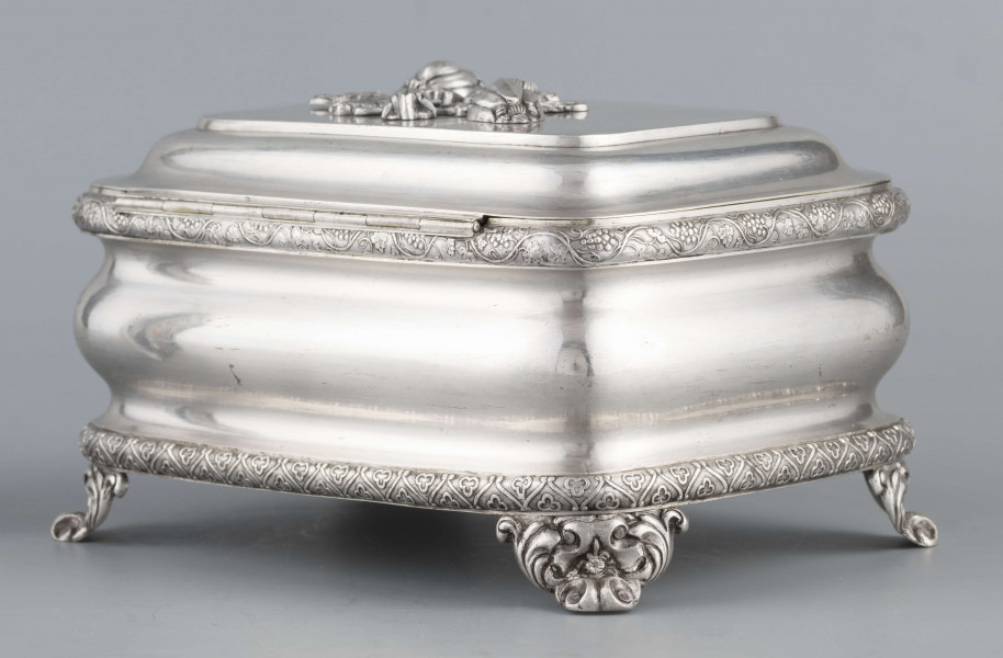 S/Mt/469/ML - Cukiernica prostokątna o zaokrągłonych narożach, profilowana, na czterech akantowych nóżkach. Brzeg dolny i górny obwiedzione półwałkiem zmoletowanej taśmy: u góry z wzorem winorośli, na dole - trójliścia.Brzeg wieczka fasetowany, z przodu lekko wywinięty tworzy uchwyt. Na wieczku nałożona półplastyczna plakieta w postaci  asymetrycznej gałązki kwiatowej. Szyld zamka stanowi sztancowana plakieta z motywem winorośli. Wnętrze złocone.
Na dnie sygnatura wypukła we wklęsłych ramkach:
- J.Suchocki
- w Lublinie
i punca z oznaczeniem próby 