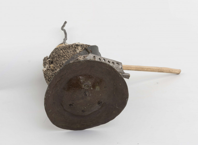 Figurka z szopki - blacharz. Kadłub drewniany na drucie. Twarz lekko ciosana. Rysy twarzy zaznaczony farbą. Blaszany kapelusz, szaro-czarna bluza, rude spodnie. Przez ramię przewieszona torba skórzana na pasku. Na piersi przymocowane narzędzia kuchenne z blachy. W prawym ręku drewniany kij.