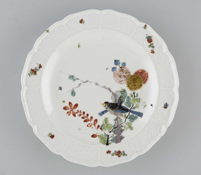 Talerz okrągły o falistym brzegu i pogrubionej krawędzi. Dno płaskie, kołnierz ukośnie odchylony pokryty reliefem plecionkowym z tzw. splotem Sułkowskiego. Dekoracja malarska w stylu Kakiemon rozmieszczona nieregularnie. Na dnie: dwa barwne ptaki (kukułki) siedzące na gałązce, nad nimi kwitnące chryzantemy. Na kołnierzu drobne gałązki kwiatowe na przemian z motylami. Barwy: błękit, czerwień, zieleń, żółcień, brąz i czerń.
 