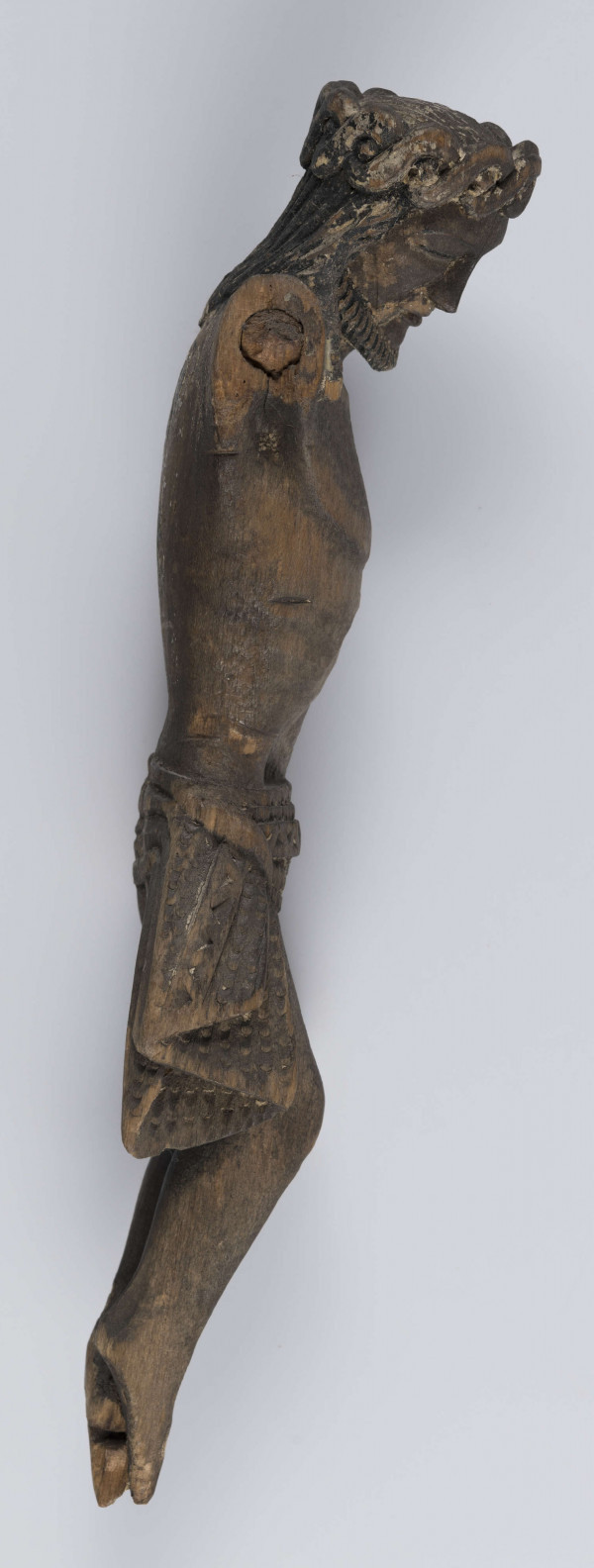 E/342/ML - Chrystus Ukrzyżowany. Stan rzeźby zły. Brak rąk i stóp. Głowa pochylona w prawo. Rysy twarz wyraziste, ostre. Głowę oplata korona cierniowa spleciona z wypukłych wałeczków. Włosy okalają twarz i opadają na ramiona. Krótka bródka, podkreślona pionowymi żłobieniami okala brodę. Piersi wyodrębnione półkolistą linią. Zaakcentowana środkowa część brzucha. Perizonium stanowi prosty, krótki płat materiału, który jest związany na prawym biodrze na węzeł, a końce jego opadają luźno. Powierzchnię perizonium wypełnia rzeźbiony ornament. Nogi proste. Podkreślone mięśnie ud i łydek. Stopy złączone.