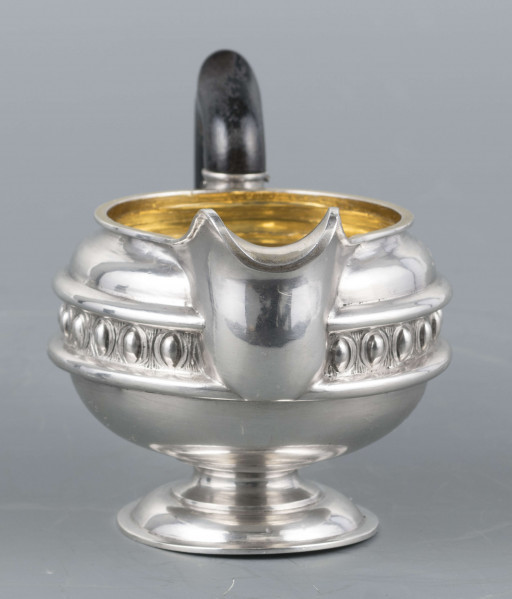 S/Mt/545/ML - Brzusiec w formie spłaszczonej kuli, pośrodku zdobiony repusowanym pasem kimationu obwiedzionego dwoma półwałkami, brzeg górny z okrągłym rantem, wylew wywinięty, zaokrąglony. Wnętrze złocone. Stopa okrągła profilowana, ucho drewniane malowane na czarno, osadzone w dwóch tulejkach . Na brzuscu pod górną krawędzią grawerowany ozdobny monogram 