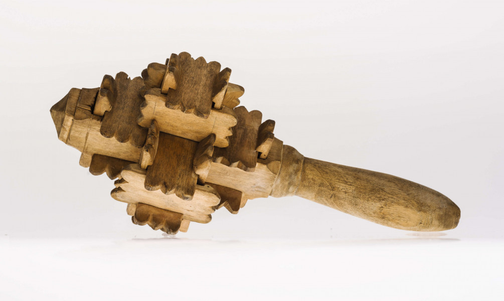 Grzechotka ta składa się z kawałeczków deseczki, rzeźbionych z brzegu i wycinanych w środku z jednej strony. Zrobiona jest bez kleju i gwożdzi. Deseczki te mają wymiary: dł. 4,5 cm szer. 2,2 cm grub. 0,5 cm. Jest ich 26. Tworzą one 6 