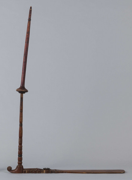 E/9283/ML - Przęślica drewniana wykonana z 3 części. Przysiadka w formie płaskiej deszczułki zwężająca się w jednym końcu i zdobiona snycerką: rozeta, motyw sercowaty, ząbki. Jej ostre zakończenie ma formę woluty/ślimaka. Przy węższym końcu osadzone pionowo ramię, toczone w pierścieniowate ozdoby. Na niego nakładany ruchomy krężel, również w toczony w pierścieniowate ozdoby. Przęślica powleczona brązowo-wiśniową farbą. Pierścieniowate elementy malowane na czarno, a na krężlu dodatkowo na srebrno.