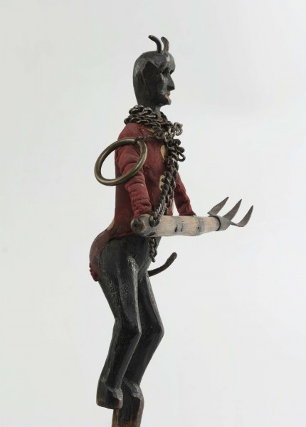 Figurka z szopki, diabeł, rzeźbiona w drewnie. Pomalowana na czarno. Ubrana w czerwony kaftan. Na szyi łańcuch. Do łańcucha doczepione widły, które diabeł trzyma obydwoma rękami. Twarz mocno modelowana, głębokie oczodoły, duże uszy, mała broda wysunięta mocno do przodu. Na głowie małe różki. Z tyłu skórzany ogon.