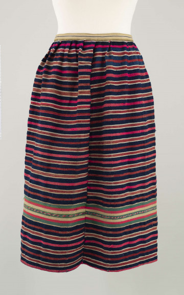 E/7351/ML - Zapaska wełniana w granatowe, czerwone, białe i amarantowe paski biegnące w poprzek. Zszyta z dwóch części – pionowy szew na przodzie. Dołem ozdobiona szerokim szlakiem dekoracyjnym, złożonym z pasków: zielonych, żółtych i amarantowych. W pasie marszczona i ujęta w oszewkę z innego materiału.