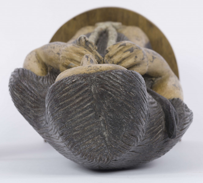 E/6353/ML - Figura drewniana, zakomponowana na postumencie, polichromowana. Postać klęcząca przedstawia św. Onufrego. Twarz płaska, trójkątna, głęboko osadzone oczy, czarne źrenice. Szerokie łuki brwiowe łączą się z wydatnym prostym nosem. Wystające kości jarzmowe. Małe usta otacza bujny zarost: broda i wąsy łączące się z bujnymi włosami, otaczającymi całą postać – na podobieństwo płaszcza. Ręce zgięte w łokciach, uniesione ku górze, łączą się końcami palców w geście modlitwy. W nieproporcjonalnie dużych dłoniach biały różaniec zakończony dużym krzyżem. Nogi masywne z dużymi płaskimi stopami. Prawą dłonią podtrzymuje sękaty kostur. W partii pasa przepasany powrozem z węzłami. 