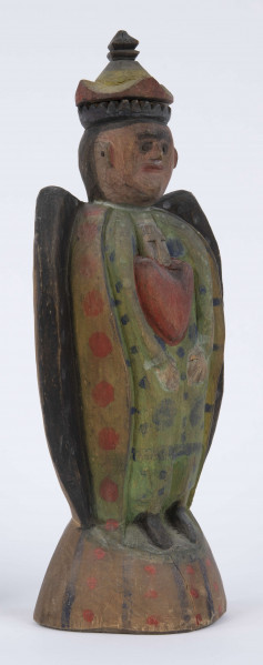 E/8100/ML - Rzeźba pełna wykonana z jednego kawałka drewna lipowego, polichromowana. Postać w hieratycznej postaci, w układzie frontalnym. Ręce wsparte na biodrach. Postać stoi na stożkowatym cokole. Na głowie korona z dwóch oddzielnych kawałków drewna, złączonych ozdobnym czopem drewnianym. Włosy czarne, ręce i twarz różowa, korona żółta z czerwonym obrzeżem, zwieńczenie czarne. Płaszcz stylizowany, przypominający skrzydła lub ornat, czarny. Szaty wewnętrzne żółte z czerwonymi plamkami. Wewnątrz długie, zielone z niebieskimi plamami. Buty czarne. Na piersiach duże otwarte serce zwieńczone czarnym krzyżem. Cokół w naturalnym kolorze drewna, ozdobiony pionowymi niebieskimi paskami i czerwonymi kropkami. Wym. cokołu: 13 x 10,5 cm. Sygnatura na spodzie (pisana): Jan Kaproń.