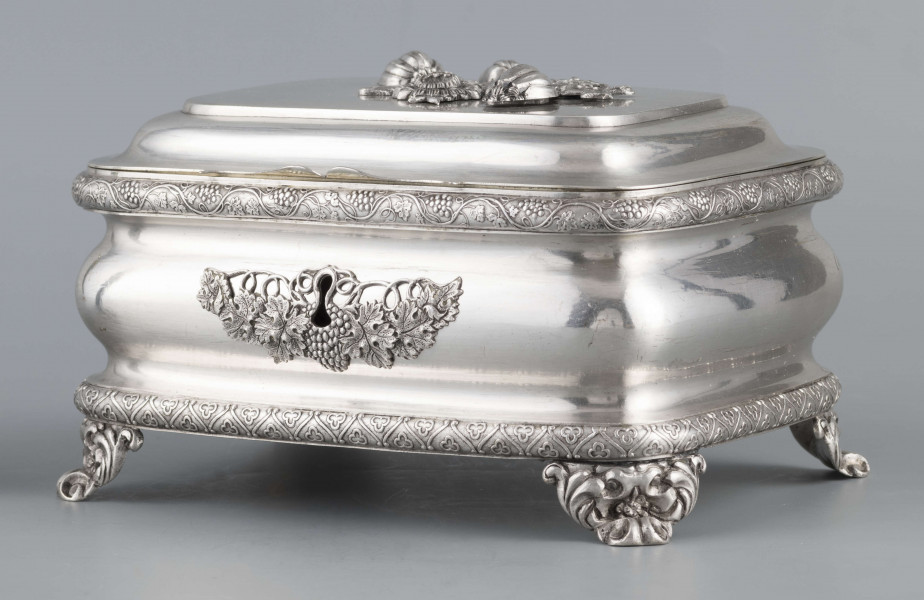 S/Mt/469/ML - Cukiernica prostokątna o zaokrągłonych narożach, profilowana, na czterech akantowych nóżkach. Brzeg dolny i górny obwiedzione półwałkiem zmoletowanej taśmy: u góry z wzorem winorośli, na dole - trójliścia.Brzeg wieczka fasetowany, z przodu lekko wywinięty tworzy uchwyt. Na wieczku nałożona półplastyczna plakieta w postaci  asymetrycznej gałązki kwiatowej. Szyld zamka stanowi sztancowana plakieta z motywem winorośli. Wnętrze złocone.
Na dnie sygnatura wypukła we wklęsłych ramkach:
- J.Suchocki
- w Lublinie
i punca z oznaczeniem próby 