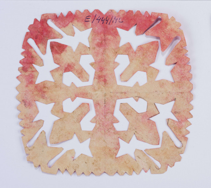 Wycinanka różowa w formie kwadratu, brzeg ząbkowany, w środku motyw krzyża o kolumnowatych ramionach. Otok z 