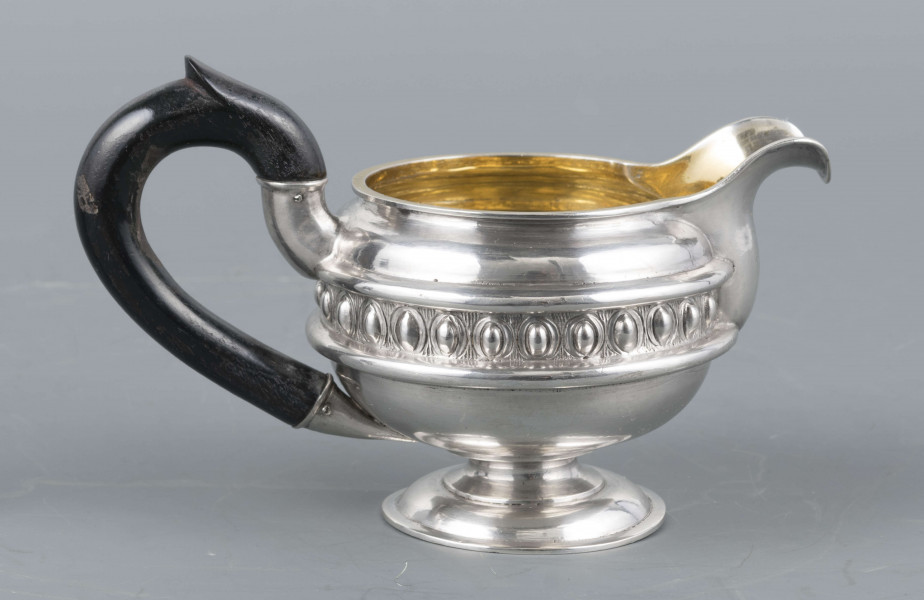 S/Mt/545/ML - Brzusiec w formie spłaszczonej kuli, pośrodku zdobiony repusowanym pasem kimationu obwiedzionego dwoma półwałkami, brzeg górny z okrągłym rantem, wylew wywinięty, zaokrąglony. Wnętrze złocone. Stopa okrągła profilowana, ucho drewniane malowane na czarno, osadzone w dwóch tulejkach . Na brzuscu pod górną krawędzią grawerowany ozdobny monogram 