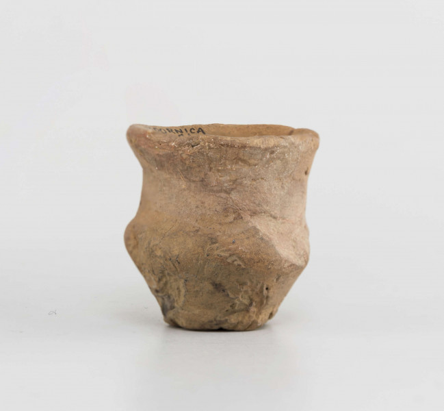 Naczynko miniaturowe. Dno małe, płaskie, wyodrębnione. Brzusiec silnie załamany. Szyjka wyodrębniona, wysoka. Krawędź zaokraglona, wychylona. Powierzchnia gładzona, na zewnętrznej odciski roślinne. Surowiec - glina z domieszką piasku. Barwa całości brunatno-pomarańczowa. Zabytek sklejany, drobne ubytki uzupełnione gipsem.
