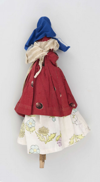 Kukiełka z szopki przedstawiająca czarownicę robiącą masło w maselnicy. Postać ubrana w jasną długą spódnicę, czerwony w koła kaftan i fartuch w szare pionowe pasy na jasnym tle. Na głowie ma granatową jedwabną chustkę wiązaną pod brodą. Twarz słabo modelowana, nos wystający, oczy namalowane farbą. Maselnica toczona, przyczepiona drutem do kukiełki.