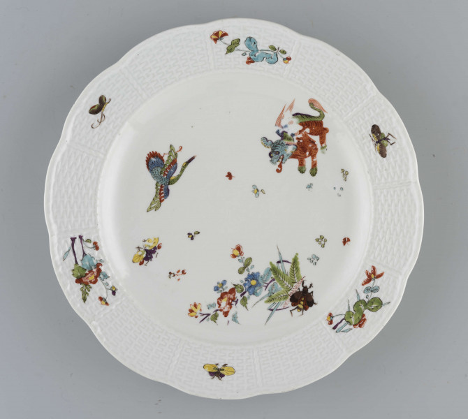 Talerz okrągły o falistym brzegu. Dno płaskie, kołnierz ukośnie odchylony pokryty reliefem plecionkowym z tzw. splotem Sułkowskiego, z podziałęm na 12 pól. Dekoracja malarska rozmieszczona nieregularnie na dnie półmiska: krzak peonii z chrabąszczem majowym, skrzydlaty smok i lecąca czapla. Na kołnierzu drobne gałązki kwiatowe na przemian z motylami. Barwy: błękit, czerwień, zieleń groszkowa i turkusowa, purpura, żółcienie, brąz i czerń.
Na spodzie sygnatura kobaltowa pod szkliwem: dwa skrzyżowane miecze.