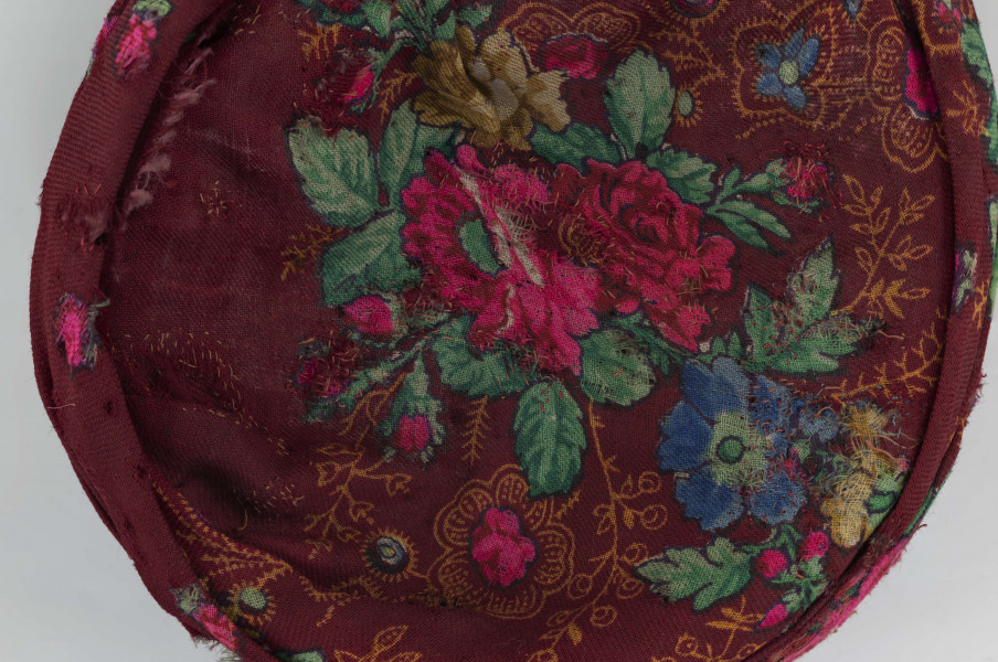 E/516/ML - Czepek mężatki. Denko wewnętrzne wykonane z plecionej siatki zielonej. Z wierzchu chustka fabryczna koloru ciemnoczerwonego w kwiaty wiązana na tekturowej obręczy. Końce chustki zwisają do tyłu.