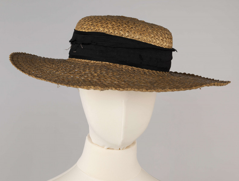 E/586/ML - Kapelusz ze słomy żytniej, o owalnym denku i płaskim rondzie. Upleciony techniką warkoczową - warkocze wąskie, ząbkowane, zszyte szarymi nićmi. Denko otoczone czarną, jedwabną wstążką o szerokości 5 cm.
