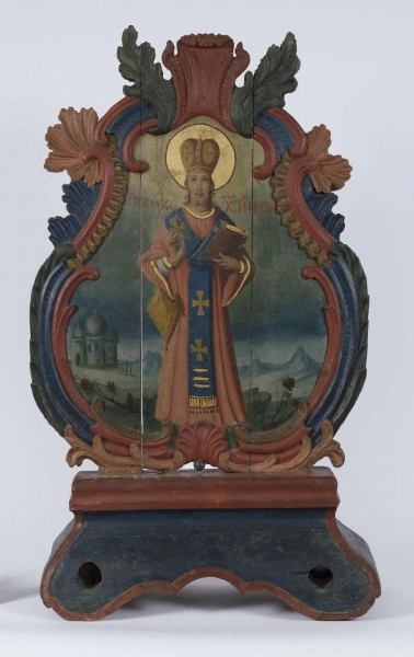 E/16801/ML - Feretron drewniany polichromowany. Z kręgu sztuki prawosławnej. W obramieniu trójlistnym ze stylizowanymi liśćmi akantu, przedstawia Matkę Bożą Chełmską i Św. Mikołaja. 
Madonna z Dzieciątkiem: w niebieskiej szacie ze złotym wykończeniem przy szyi, czerwonym płaszczu, złotej koronie. Na prawym ramieniu trzyma Dzieciątko, w biało-szarej szacie i złotej koronie. Wzrok postaci skierowane ku sobie. Wokół głów – złote nimby. Karnacja cielisto-brązowa. Tło ciemnobrązowe. Po obu stronach głów postaci litery.
Św. Mikołaj: postać stojąca w czerwono-niebieskiej szacie ze złotymi lamowaniami. W lewej, zgiętej w łokciu ręce – księga, brązowa ze złotymi kartami. Prawa ręka zgięta i uniesiona w geście błogosławieństwa; pod nią torba. Na szyi – łańcuch z krzyżem. Na głowie biskupia korona, a wokół niej złoty nimb. Po obu stronach postaci, na wysokości ramion, napisy w j. greckim. W tle pejzaż ze wzniesieniem i roślinnością, a po lewej stronie przedstawienia – cerkiew. 
Kolory obramienia feretronu: ceglasty, czerwony, granatowy, ciemnozielony. 

Konserwacja: 1999-2000