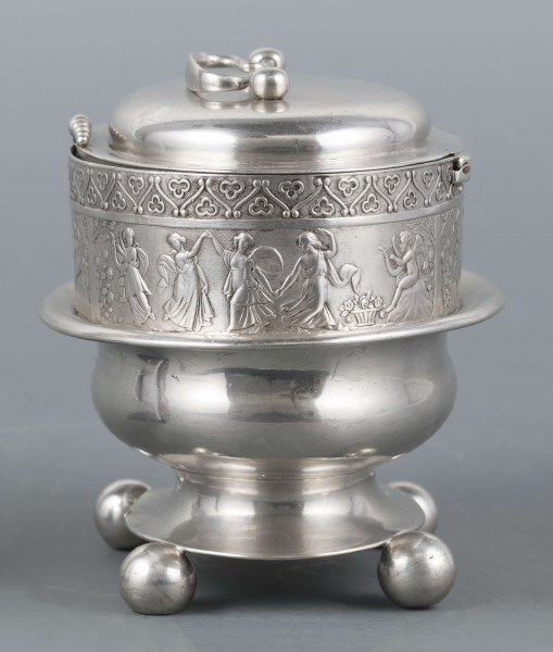 S/Mt/363/ML - Cukiernica owalnana niskiej stopie z czterema kulistymi nóżkami, z pokrywką w formie wieczka.
Podzielona na dwie części : 
- część dolna lekko wybrzuszona, o gładkiej powierzchni, kończy się w połowie wysokości wywiniętym kołnierzem; - część górna prosta uformowana jest z moletowanej taśmy, na której powtarza się trzykrotnie scenka antyczna: po rawej siedzący pod drzewem amorek gra na lirze, po lewej stoi grająca na lirze kobieta, pomiędzy nimi tańczą trzy inne.Górną krzwędź obiega pas stylizowanych neogotyckich trójliści.