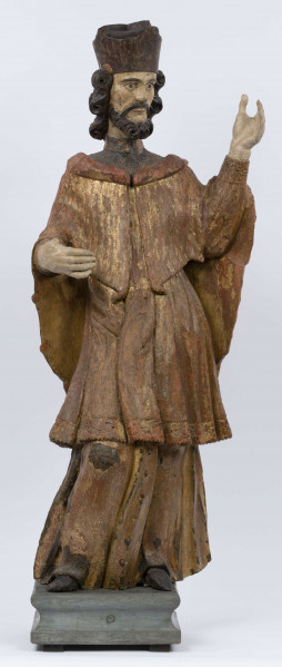 E/16816/ML - Rzeźba drewniana, pełna, polichromowana, przedstawiająca św. Jana Nepomucena. Kompozycja frontalna. Postać stojąca w kontrapoście – prawa noga zgięta i wysunięta do przodu. Sylwetka przechylona na prawo. Lewa ręka zgięta w łokciu i wysunięta do przodu. Prawa zgięta, uniesiona do góry. Brak atrybutów (krzyża i palmy) w dłoniach.
Postać ubrana w sutannę, komżę drapowaną w fałdy i zakończoną koronką, płaszcz z kapturem. Ślady złoceń na partii ubrania. Głowa skierowana na prawo. Twarz podłużna (kolor kremowy), usta proste, oczy z zaznaczonymi na ciemno tęczówkami, nos prosty, lekko zaznaczone kości policzkowe. Wolutowe pukle brody i włosów, symetryczne. Na głowie ciemnobrązowy biret. Stopy wystające spod sutanny.

Konserwacja: 2001 r.