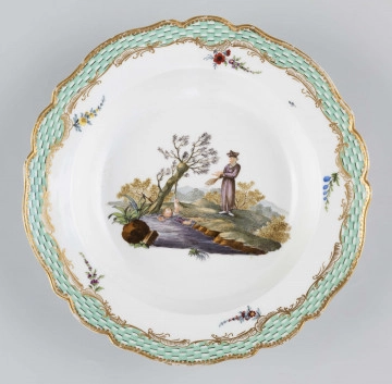 S/CS/1580/ML - Talerz głęboki o falistym wykroju brzegu. Na dnie malowana barwna miniatura przedstawiajaca scenkę w pejzażu: chłopiec wpadł do strumienia i trzyma się gałązki wierzby rosnacej na brzegu, obok stoi nauczyciel z rózgą w ręce. Na kołnierzu malowana mozaika w kolorze zieleni miedziowej, obramowana od środka złotymi rocaille'ami z piecioma rzuconymi gałązkami. 
Na spodzie napis wykonany naszkliwnie purpurą: 
