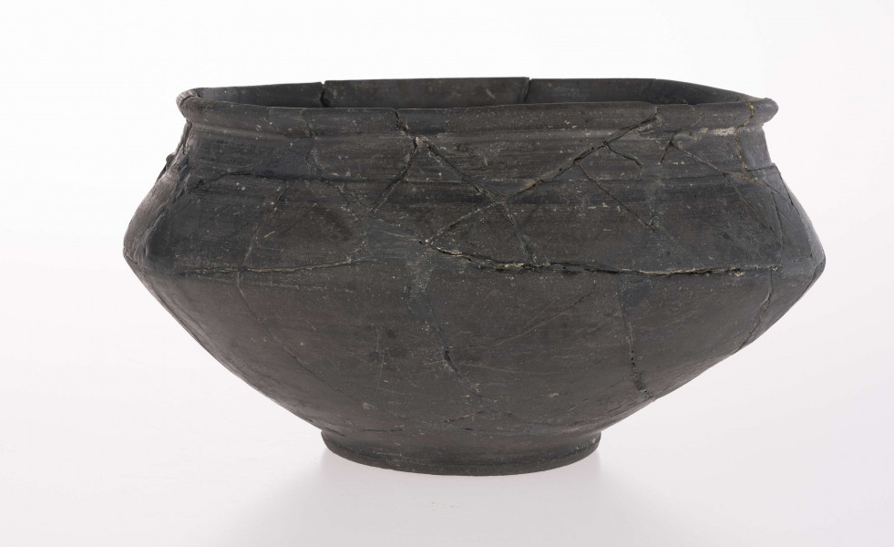 Naczynie wazowate - dwustożkowate; dno lekko wklęsłe z dołeczkiem w środku, wyraźnie wyodrębnione niewielką stopką; brzusiec dwustożkowaty, ostro profilowany; miejsce przejścia brzuśca w szyję zaznaczone wypukłą dookolna listwą; szyja niska, cylindryczna; wylew zaokrąglony, wywiniety na zewnatrz; górna część brzuśca zdobiona dookolnym rzędem narysowanych 