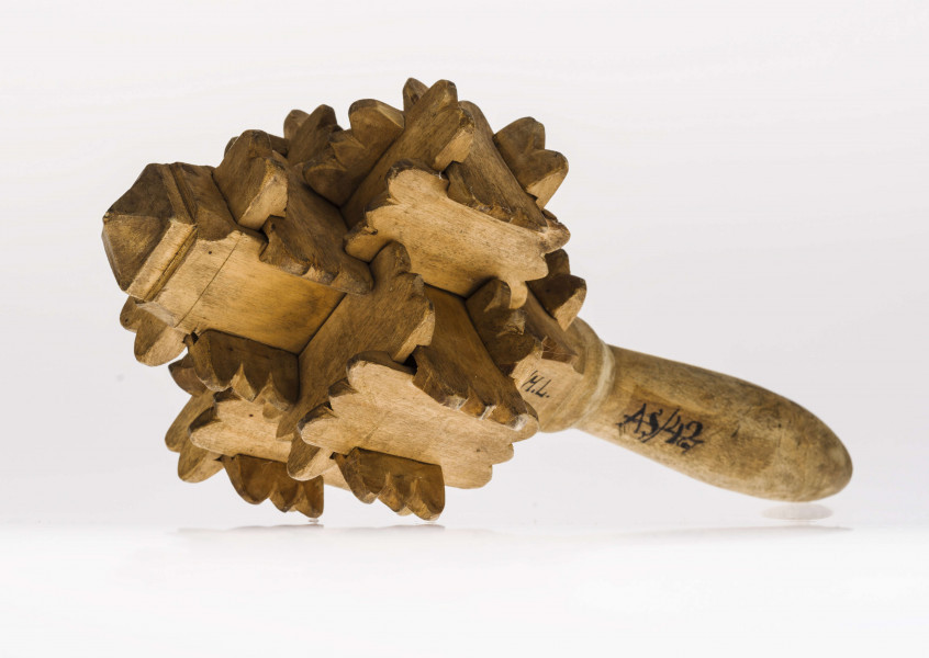 Grzechotka ta składa się z kawałeczków deseczki, rzeźbionych z brzegu i wycinanych w środku z jednej strony. Zrobiona jest bez kleju i gwożdzi. Deseczki te mają wymiary: dł. 4,5 cm szer. 2,2 cm grub. 0,5 cm. Jest ich 26. Tworzą one 6 