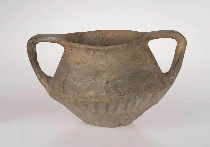 Naczynie wazowate, dwustożkowe z dwoma taśmowatymi uchami. Nad załomem brzuśca zdobienie w postaci linii rytych wypełnionych ukośnym kreskowaniem. Powierzchnia brunatna. Typ III/3 wg T. Liany.