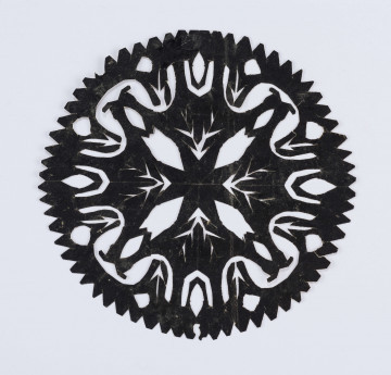 Wycinanka czarna z glansowanego papieru, w środku krzyż o ramionach wachlarzowatych, żyłkowanych jak liście, pomiędzy nimi ażurowane owale i jezyczki. Wycinanka naklejona na biały papier i wraz z nim na biały papier rysunkowy.