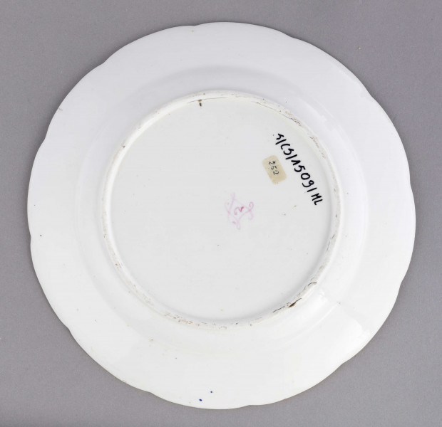 Talerz płytki o falistym wykroju brzegu, przy krawędzi plastyczne kanelowanie podkreślone błękitnym paskiem. Dekoracja malowana wielobarwnie: na całej powierzchni swobodnie rozrzucone różnej wielkości bukiety i gałązki kwiatowe.