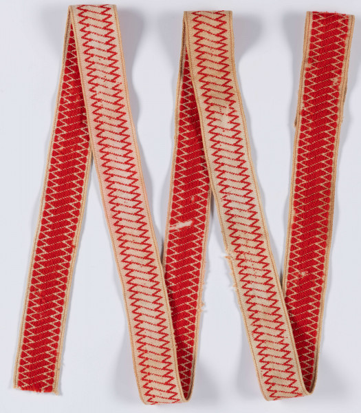 E/12133/ML - Kolorowa krajka. Na bawełnianym płótnie tkanym splotem prostym znajduje się przetykany ornament geometryczny koloru czerwonego.

