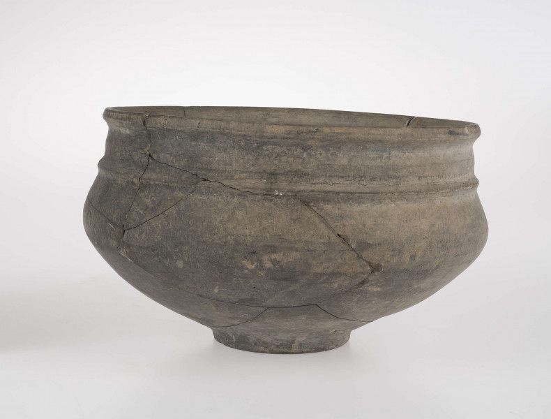 Naczynie o wklęsłym dnie, z dołkiem w centralnej części. Dno wyodrębnione niewysoką stopką. Brzusiec łagodnie profilowany. Szyjka podkreślona plstyczną listwą, w części środkowej nieco wypukła. Krawędź wylewu delikatnie wywinięta na zewnątrz. 