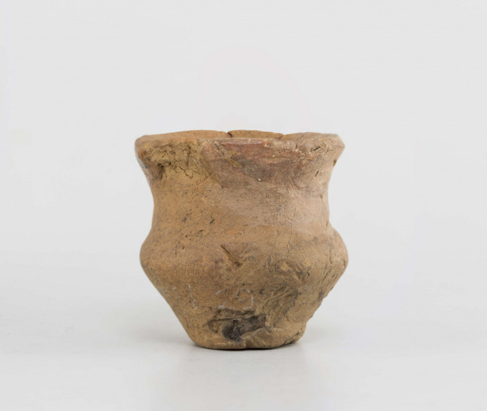 Naczynko miniaturowe. Dno małe, płaskie, wyodrębnione. Brzusiec silnie załamany. Szyjka wyodrębniona, wysoka. Krawędź zaokraglona, wychylona. Powierzchnia gładzona, na zewnętrznej odciski roślinne. Surowiec - glina z domieszką piasku. Barwa całości brunatno-pomarańczowa. Zabytek sklejany, drobne ubytki uzupełnione gipsem.