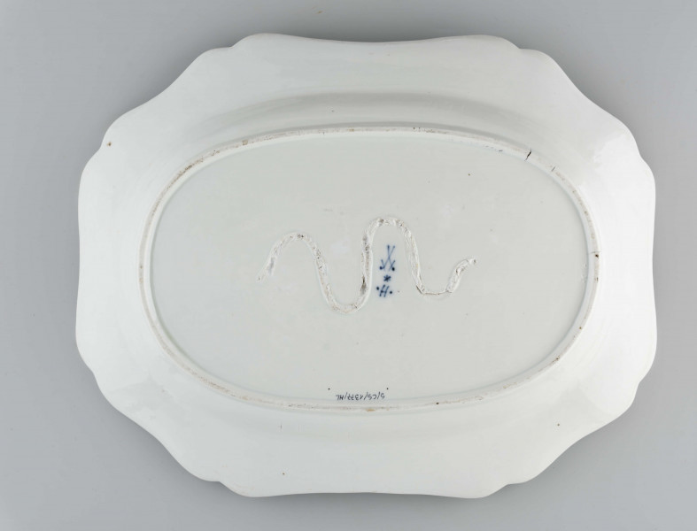 Półmisek owalny, kołnierz gładki o brzegu wykrojonym faliscie. Malowany podszkliwnie kobaltem we wzór tzw. cebulowy, na dnie wieksza kompozycja ze stylizowanych gałązek z kwiatami. Dno wzmocnione od spodu esowatym pasmem z masy porcelanowej.
 