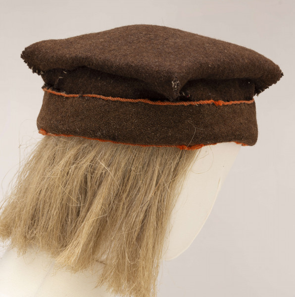 Czapka męska rogatywka szyta ręcznie z samodziałowego sukna w kolorze brązowym. Jeden pas stanowi otok., drugi tej samej szerokości jest wywinięty na wierzch i obszyty na dolnej i górnej krawędzi pomarańczowym wełnianym sznureczkiem. Górna cześć czapki wykonana z kwadratowego płata z wywiniętymi narożnikami, które po zszyciu i przyszyciu do otoka tworzą płaskie kwadratowe denko, o wym. 20 x 20 cm. Noszona do sukmany.