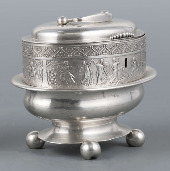 S/Mt/363/ML - Cukiernica owalnana niskiej stopie z czterema kulistymi nóżkami, z pokrywką w formie wieczka.
Podzielona na dwie części : 
- część dolna lekko wybrzuszona, o gładkiej powierzchni, kończy się w połowie wysokości wywiniętym kołnierzem; - część górna prosta uformowana jest z moletowanej taśmy, na której powtarza się trzykrotnie scenka antyczna: po rawej siedzący pod drzewem amorek gra na lirze, po lewej stoi grająca na lirze kobieta, pomiędzy nimi tańczą trzy inne.Górną krzwędź obiega pas stylizowanych neogotyckich trójliści.