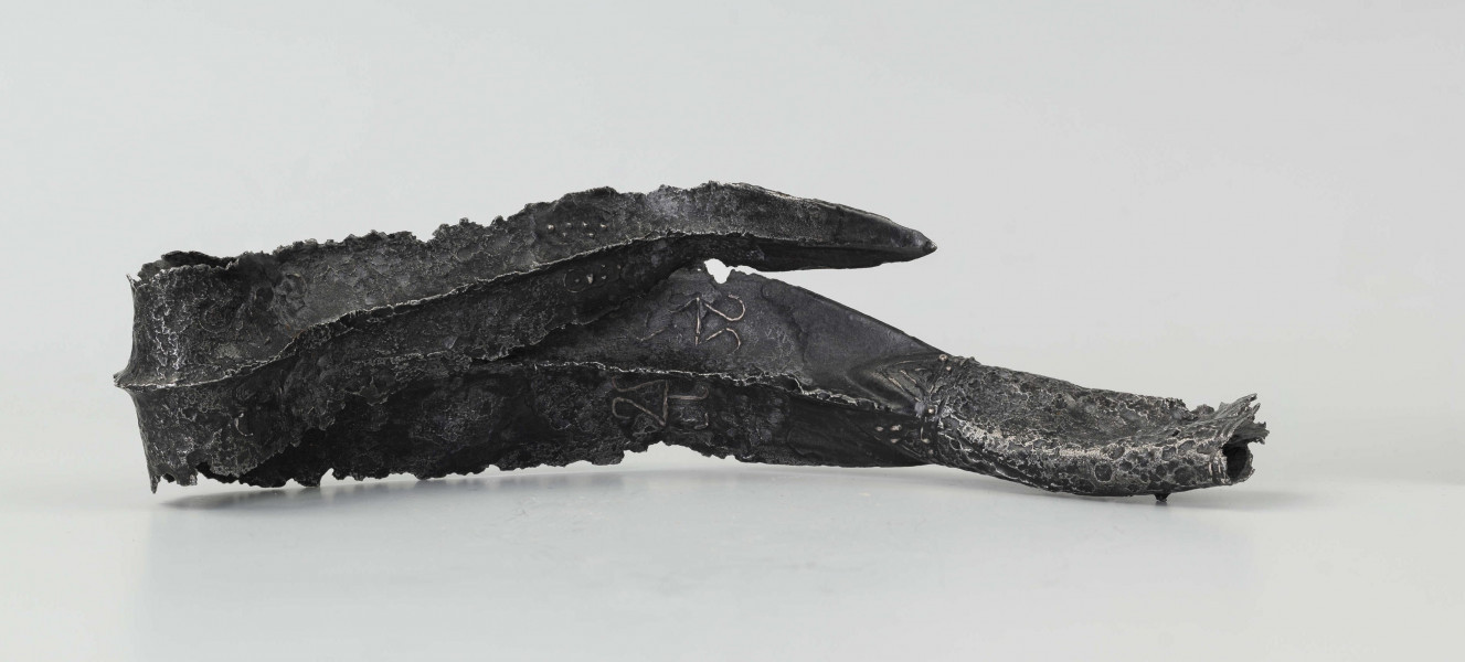 Żelazny grot broni drzewcowej zdobiony wyjątkową, srebrną inkrustacją jest częścią uzbrojenia włożonego do grobu ciałopalnego wojownika z początku III w. n.e. 
Grób przedstawiciela ludności kultury przeworskiej został odkryty przypadkowo w 1959 roku. 
Oprócz trzech grotów, pochówkowi wojownika towarzyszyły: żelazne umbo, dwie ostrogi, tok brązowy (prawdopodobnie okucie drzewca oszczepu) a także żelazny miecz z miedziana inkrustacją wyobrażającą rzymskich bogów. Pochowany na terenie obecnej wsi Podlodów wojownik należał do elity wojskowej przedstawicieli kultury przeworskiej. Liść grotu jest smukły i długi, a u podstawy cylindrycznej i krótkiej tulejki znajduje się żeberko. Na obydwu częściach grotu znajdują się zdobienia inkrustowane srebrem - znaki o znaczeniu symbolicznym: trójkąty sferyczne, punkty, podwójne widełki. Przypominają one symbole religijne (ewentualnie znaki magiczne lub własnościowe) - tamgi. Niektórzy badacze zakładają, że mogły one zostać przejęte przez Sarmatów. 
Wymiary dodatkowe: szer. 4,0 cm 