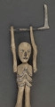 E/319/ML - Figurka z szopki, przedstawiająca śmierć, wykonana z drzewa, pomalowana białą farbą. Głowa o kształcie trójkątnym, wydłużonym. Oczy, nos i usta wydrążone i pomalowane srebrną farbą. Tułów krótki z zaznaczonymi plastycznie i zaznaczonymi srebrną i czarną farbą. Ręce ruchome w ramieniu, osadzone na drucie, w łokciu nieco zgięte z zaznaczonym plastycznie stawem łokciowym. Nogi proste, bez stóp, z silnie zgrubiałymi kolanami, z wyrzeźbionymi gwiazdkami pomalowanymi srebrną farbą. W rękach figurka trzyma kosę z drutu i cienkiej blaszki. Do ramienia przymocowany jest drut przechodzący z tyłu i założony za klamerkę wmontowaną w prawą nogę z tyłu. Drucik ten umożliwia poruszanie rękami figurki w czasie przedstawienia. W prawej nodze umocowany jest drut o haczykowatym zakończeniu.