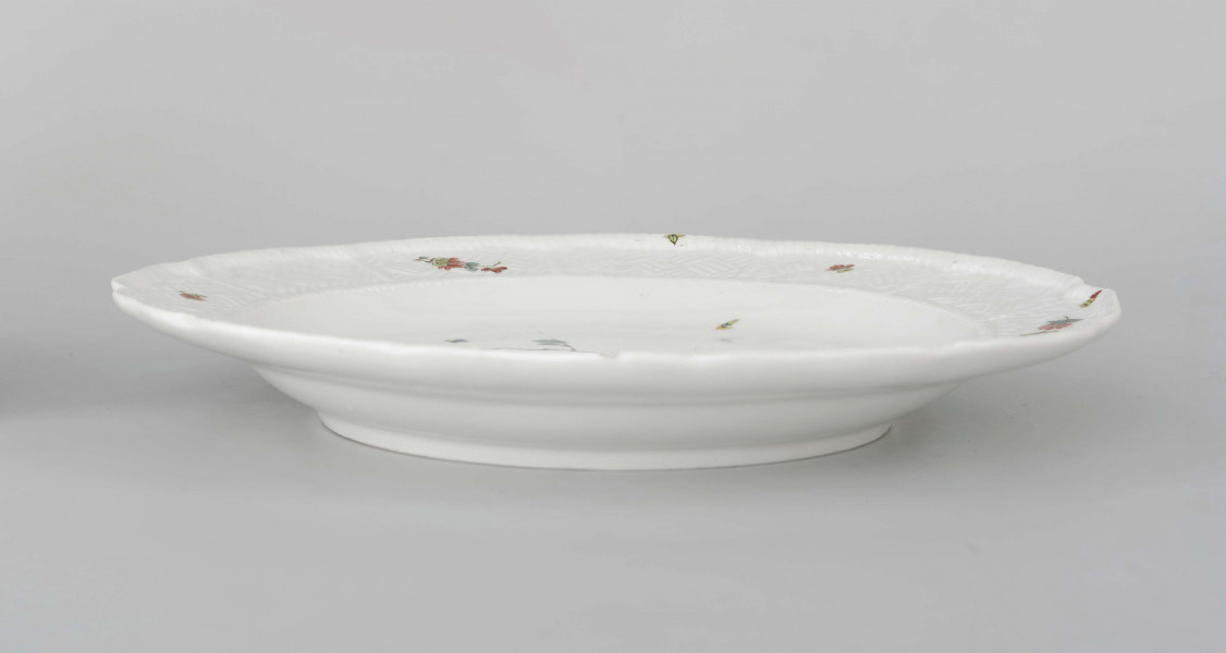 Talerz okrągły o falistym brzegu i pogrubionej krawędzi. Dno płaskie, kołnierz ukośnie odchylony pokryty reliefem plecionkowym z tzw. splotem Sułkowskiego. Dekoracja malarska w stylu Kakiemon rozmieszczona nieregularnie. Na dnie: dwa barwne ptaki (kukułki) siedzące na gałązce, nad nimi kwitnące chryzantemy. Na kołnierzu drobne gałązki kwiatowe na przemian z motylami. Barwy: błękit, czerwień, zieleń, żółcień, brąz i czerń.
 