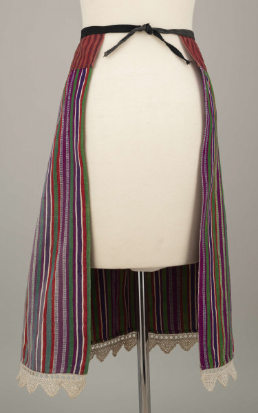 E/8132/ML - Fartuch wełniany szyty maszynowo. Wykonany z materiału samodziałowego tkanego w pionowe paski, w kolorach: czerwonym, białym, szafirowym, bordowym, zielonym. Uszyta z prostokątnego kawałka materiału, do którego doszyto z obu stron kliny. U góry fartuszek przedłużony przez wszycie kawałka materiału szer. 7 cm, w pasy czerwono-granatowe. W talii wszyty w pasek z czarnego materiału, szer. 2 cm, zakończony troczkami. Dół fartuszka zdobi biała koronka szer. 5 cm.