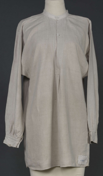 E/7980/ML - Koszula męska z lnianego, szarego płótna. Szyta ręcznie. Kołnierzyk to wąska oszewka z bawełnianego płótna. Z przodu rozcięcie zapinane na 3 guziczki wzmocnione plisą z podwójnego kawałka płótna. Rękawy długie, ujęte w mankiet, zapinany na guziczek. Pod pachami wszyte prostokątne kawałki tkaniny, zw. tokami.