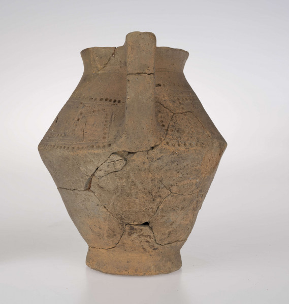 Dzban ostro profilowany, z prostym, odgiętym na zewnatrz brzegiem podkreślonym rowkiem, ostro zaznaczonym załomem brzuśca i wyodrębioną stopką. Ucho dzbana jest taśmowate, kolankowato zgięte, z przewierconym kanalikiem. Ponad załomem brzuśca naczynie zdobione jest ornamentem blankowym, który tworzy para równolegle rytych linii wypełnionych dołkami. Całość ujęta górą i dołem w wątek linii rytej i rzędu dołków. 
