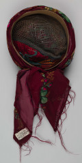 E/516/ML - Czepek mężatki. Denko wewnętrzne wykonane z plecionej siatki zielonej. Z wierzchu chustka fabryczna koloru ciemnoczerwonego w kwiaty wiązana na tekturowej obręczy. Końce chustki zwisają do tyłu.