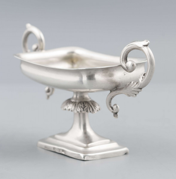 S/Mt/57/ML - Stopa prostokątna, wysklepiona, przechodząca w trzon z owalnym kapturkiem sztancowanym we wzór akantu. Czarka prostokatna o zaokrąglonych narożach i wywinietym brzegu, z dwoma uchami na krótszych bokach. Ucha wolutowe zdobione listkami. 