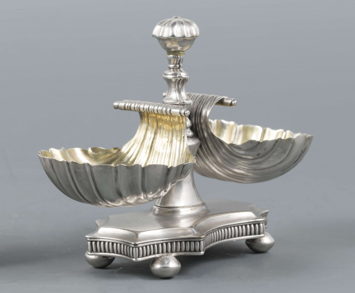 S/Mt/494/ML - Solniczka składa się z dwóch czarek w formie muszli połączonych z pionowym, profilowanym uchwytem o zwieńczniu w formie makówki ustawionym na wydłużonej ośmiobocznej podstawie o wklęsłych bokach. Krawędź podstawy fasetowana, boki karbowane, cztery nóżki w kształcie spłaszczonych kulek. Wnetrze muszli złocone.
Na dnie podstawy sygnatura kursywą w owalnych ramkach:
- J.Gałecki
- w Lublinie
- punca owalna z przedstawieniem dłoni (sygnatura pomocnicza)
- wężyk probierczy
- znak probierni warszawskiej z próbą 