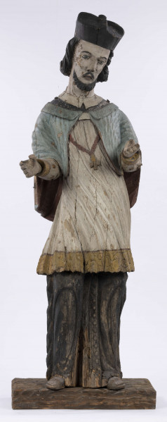 E/8422/ML - Rzeźba drewniana, pełna, polichromowana, przedstawiająca św. Jana Nepomucena. Zakomponowana frontalnie, z rękoma zgiętymi w łokciu i lekko rozłożonymi. Twarz owalna, pomalowana białą farbą. Małą broda i krótkie czarne wąsy. Nos krótki, prosty. Oczy owalne podkreślone czarnym konturem. Brwi łukowate, wąskie, czarne. Włosy czarne, ułożone w pukle. Na głowie czarny biret. Długa czarna sutanna, biała komża ozdobiona u dołu złotą koronką. Na piersiach krzyż, zawieszony na łańcuchu. Na komżę narzucona jasnoniebieska peleryna. Stopy lekko rozstawione. Obuty w sandały o jednym pasku. 

Konserwacja: 1990 r.