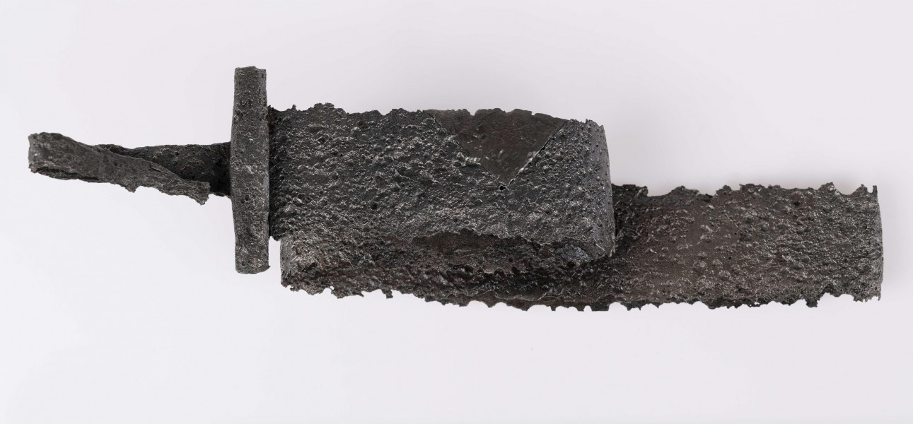 Miecz żelazny, obosieczny, bez strużyn. U podstawy trzpienia znajduje się krótki, prosty w przekroju czworoboczny jelec. Kolec prosty na końcu rozklepany. Miecz rytualnie zgięty.