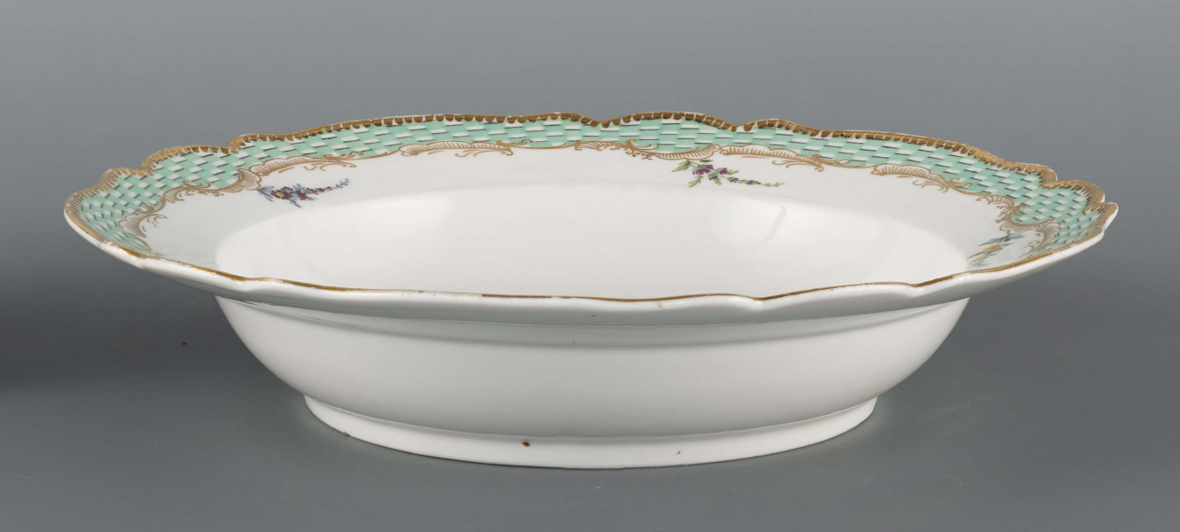 S/CS/1580/ML - Talerz głęboki o falistym wykroju brzegu. Na dnie malowana barwna miniatura przedstawiajaca scenkę w pejzażu: chłopiec wpadł do strumienia i trzyma się gałązki wierzby rosnacej na brzegu, obok stoi nauczyciel z rózgą w ręce. Na kołnierzu malowana mozaika w kolorze zieleni miedziowej, obramowana od środka złotymi rocaille'ami z piecioma rzuconymi gałązkami. 
Na spodzie napis wykonany naszkliwnie purpurą: 