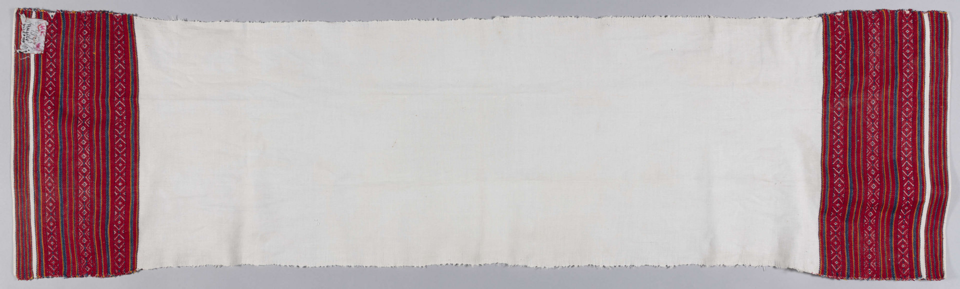 E/4943/ML - Ręcznik lniany, z haftem na obu końcach. Haft tkany na warsztacie. Wzór tworzą pasy w kolorach: czerwonym, pomarańczowym i granatowym oraz szlak złożony z rombów i serduszek. Szerokość kolorowego szlaku - 16 cm.