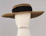 E/586/ML - Kapelusz ze słomy żytniej, o owalnym denku i płaskim rondzie. Upleciony techniką warkoczową - warkocze wąskie, ząbkowane, zszyte szarymi nićmi. Denko otoczone czarną, jedwabną wstążką o szerokości 5 cm.
