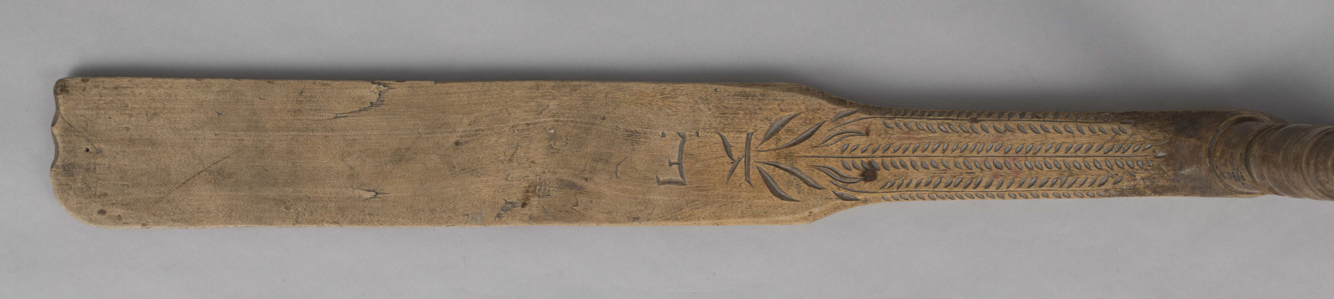 E/8019/ML - Przęślica krężołkowa z drewna brzozowego składa się z cienkiej deski – przysiadki, w której przy jednym końcu osadzona jest pionowa beleczka zw. piórem, z nasadzonym od góry ruchomym krężlem w kształcie wydłużonego stożka. Deseczka przysiadki o kształcie prostokątnym lekko zwężającym, od ok. połowy swej długości w kierunku pióra, i zakończonym głową zwierzęcą – psa. Pióro i krężel ozdobnie toczone. Krężel ma kształt stożka z rozszerzoną podstawą, w której znajduje się stożkowaty otwór, do osadzenia krężla na piórze. Dekoracja snycerska ryta znajduje się na zwężającej części przysiadki. Część zdobiona oddzielona małym stopniem. Grubość przysiadki w części zdobionej 2x większa od pozostałej części. Dekoracja snycerska tworzy ornament roślinny w postaci trzech ulistnionych drobno gałązek. Na zakończeniu ornamentu znajdują się ryte liście oraz inicjały „K.F.”. Głowa psa zdobiona drobnymi nacięcia. Zakończenie przysiadki wycięte faliście.