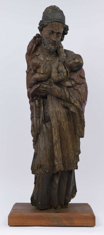 E/17554/ML - Rzeźba drewniana, pełna, z resztkami polichromii, przedstawiająca św. Józefa z Dzieciątkiem. Kompozycja frontalna. Postać stojąca, ubrana w długą szatę wykończoną ozdobną szatę wykończoną ozdobną koronką przy rękawach, drapowane w pionowe fałdy. Na ramionach  płaszcz, również wykończony koronką. Tył postaci modelowany gładko. Prawa ręka, wyciągnięta wzdłuż ciała, trzyma kwiat, który wystaje ponad ramię. Na lewej zgiętej ręce – Dzieciątko, które prawą ręką trzyma się szyi św. Józefa. Dzieciątko nagie, w pieluszkach. 
Twarz świętego skierowana w stronę Dzieciątka, pochylona w prawo. Pociągła. Nos posty. Usta lekko zaznaczone. Oczy lekko przymknięte. Bruzdy na czole i policzkach, misterne pukle brody i włosów. Na głowie rodzaj czapki, ściśle przylegającej. Postać świętego bez stóp. Liczne spękania i ubytki fragmentów.

Konserwacja: 1988 r.